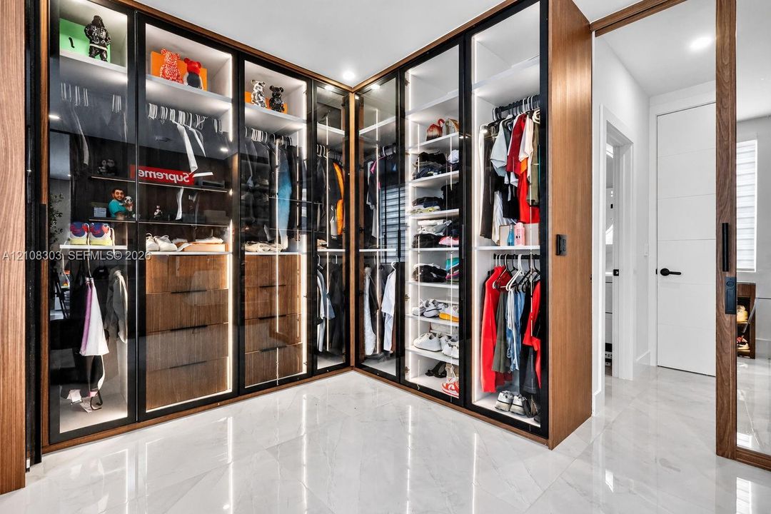 Custom built-in wardrobe featuring full-height glass-paneled doors, integrated LED accent lighting, wood-finish cabinetry, matte black hardware, and polished tile flooring