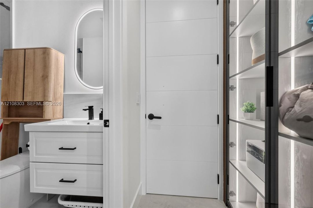 Bathroom featuring a white vanity with matte black hardware, integrated backlit oval mirror, wood-tone wall-mounted cabinet, and built-in shelving with vertical LED lighting