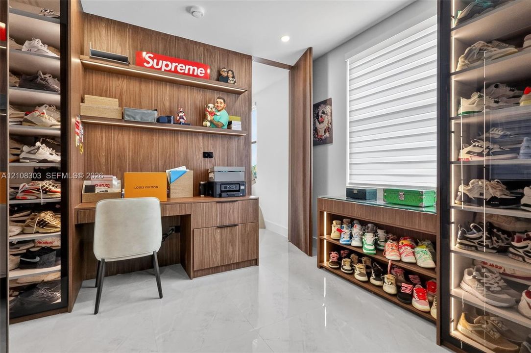 Custom wood-finish cabinetry featuring integrated shelving, built-in desk with drawer storage, glass-front display cases with internal lighting, and light-tone tile flooring