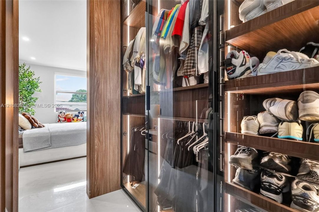 Custom walk-in closet featuring floor-to-ceiling wood-finish cabinetry, glass-front doors, and integrated vertical LED lighting