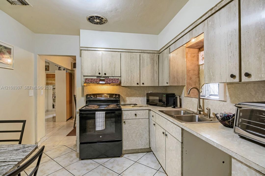 Kitchen featuring cabinetry with a stone-finish facade, stainless steel dual-basin sink, high-arc faucet, and tiled flooring