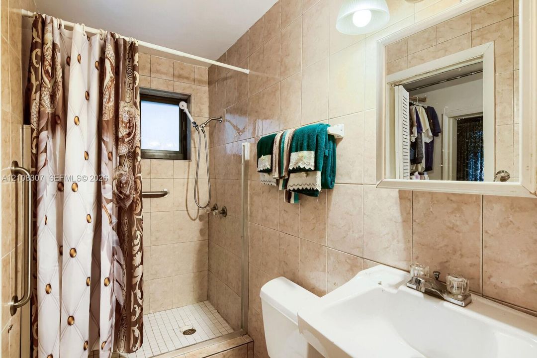 Bathroom featuring full-height wall tiling, a walk-in shower with a glass door, a pedestal sink with a dual-handle faucet, and a wall-mounted medicine cabinet