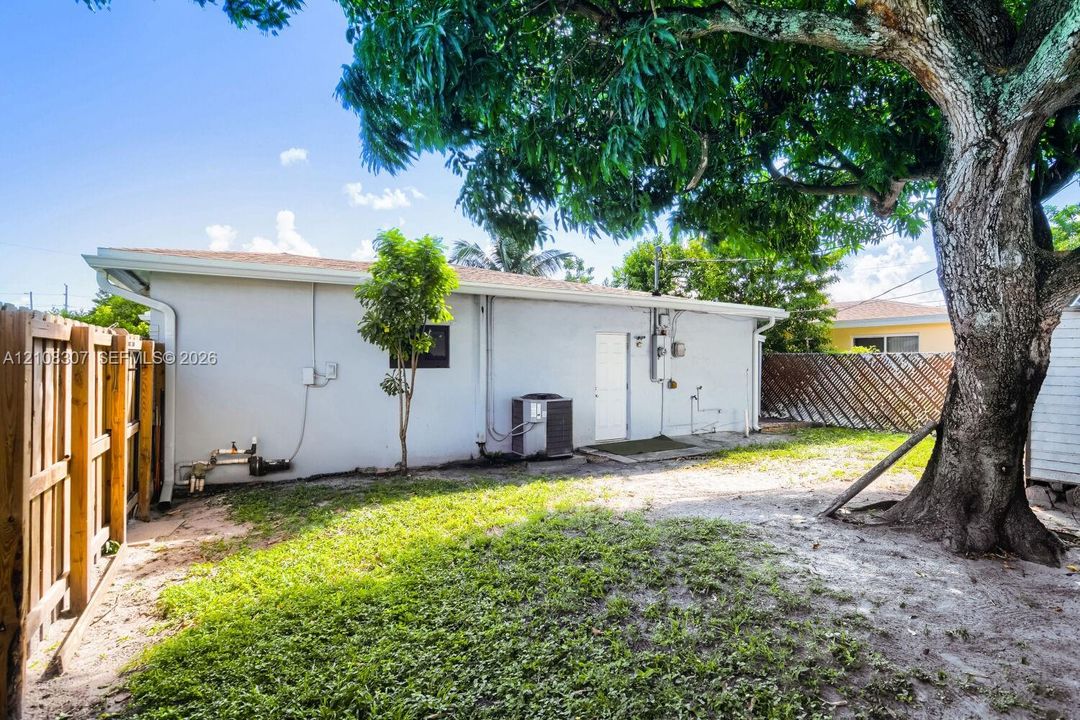 Fenced backyard featuring mature trees, grass area, and exterior home access