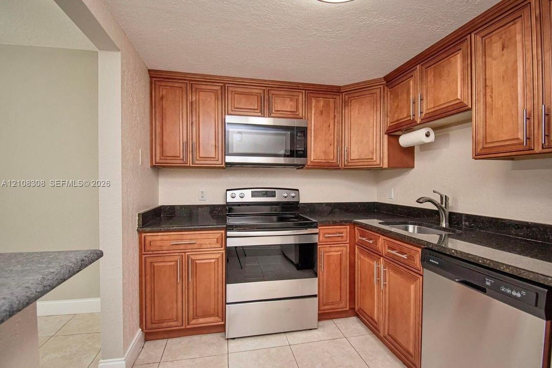 Kitchen featuring wood cabinetry, stone-finish countertops, stainless steel appliances, a double-basin sink, and tile flooring