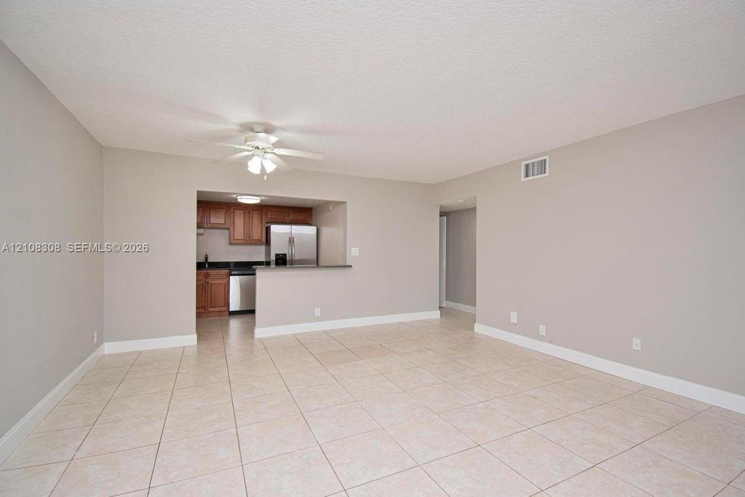 Open living area featuring neutral wall paint, tile flooring, a ceiling fan with light kit, and a kitchen pass-through with a peninsula
