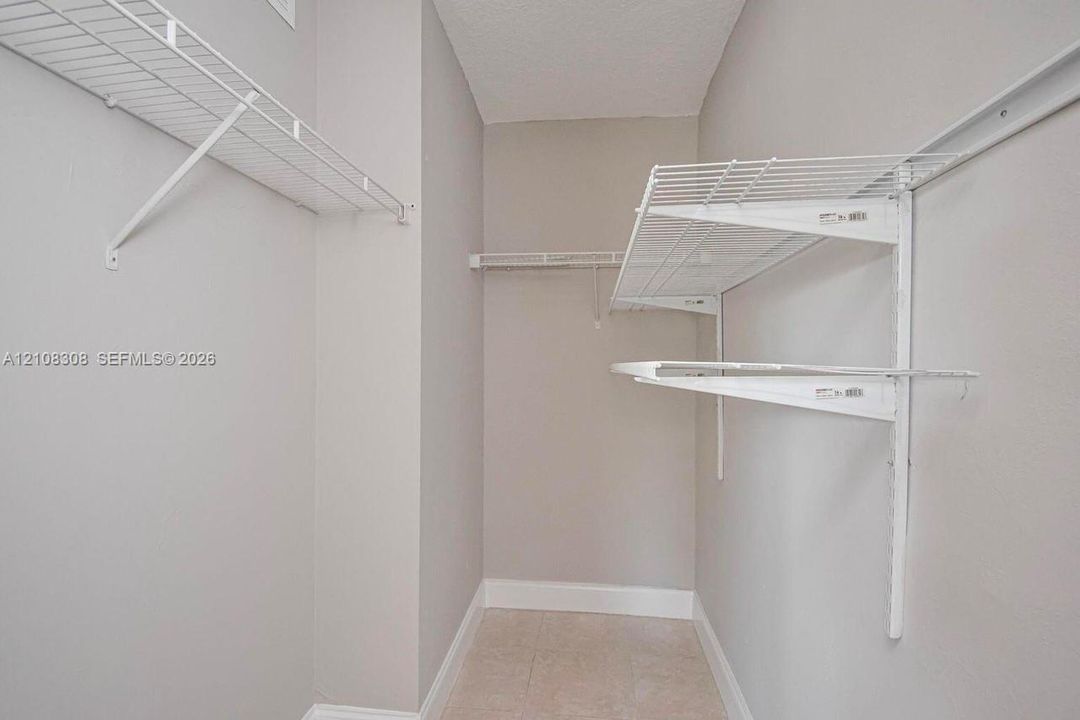 Walk-in storage space featuring neutral wall paint, tile flooring, and white wire shelving systems