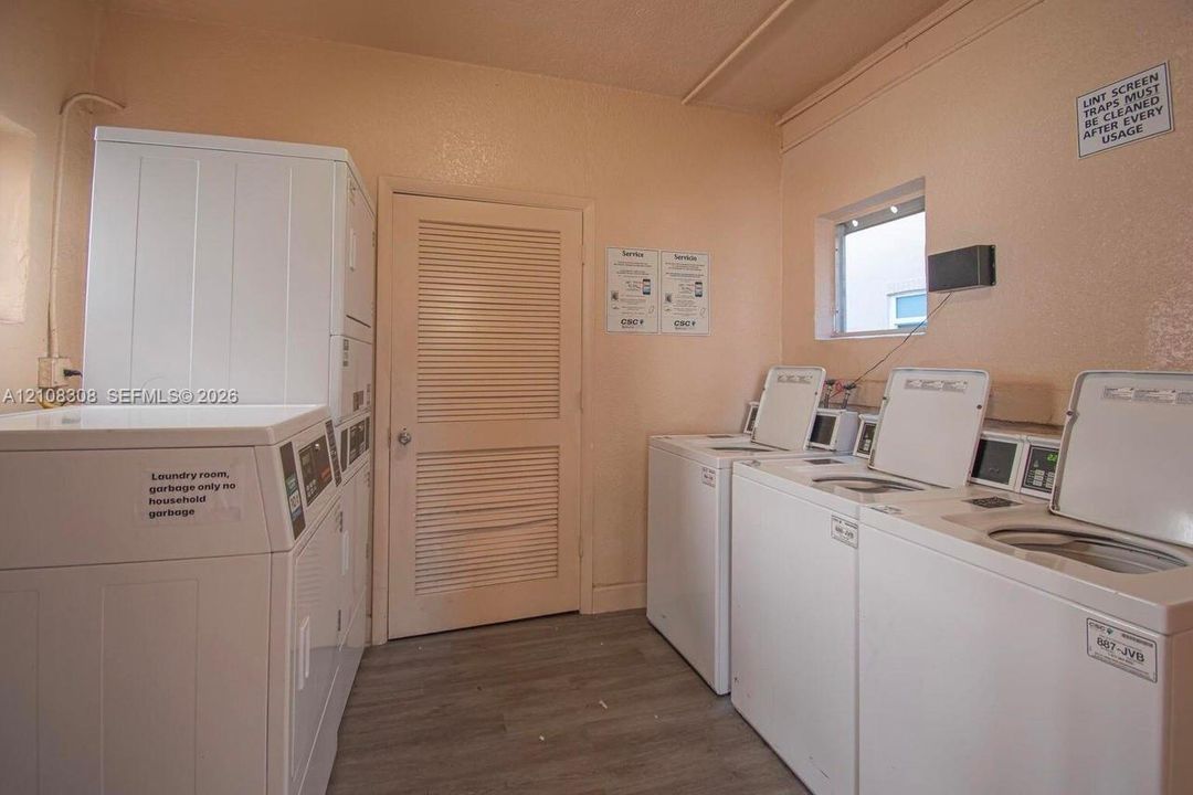 Laundry facility featuring multiple top-load washers, a stackable dryer unit, louvered interior door, and wood-finish flooring