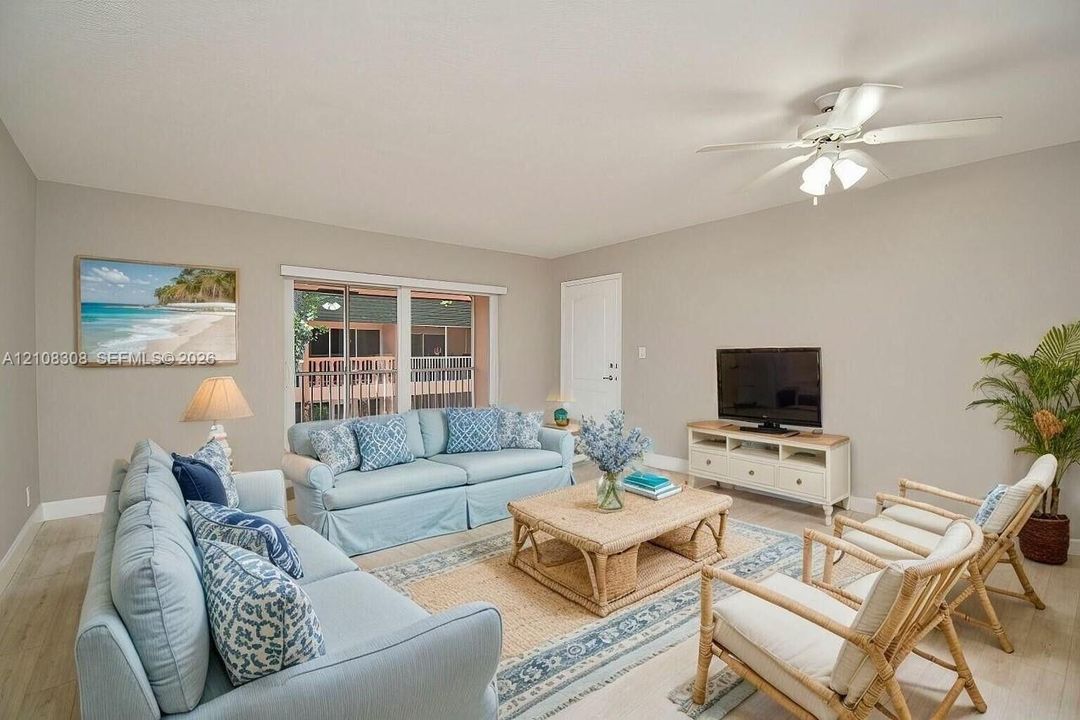 Living area featuring wood-finish flooring, a ceiling fan with integrated lighting, and a large sliding glass door with horizontal blinds