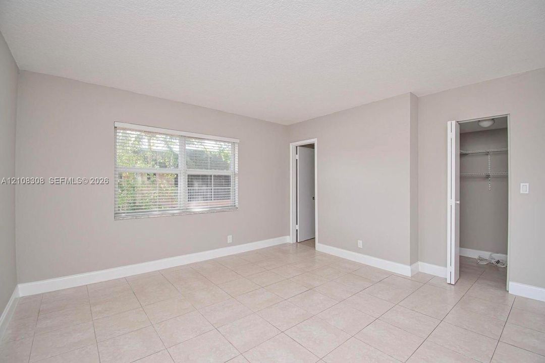 Neutral-toned interior featuring large-format tile flooring, a dual-pane window with adjustable blinds, and a built-in closet with folding doors and wire shelving