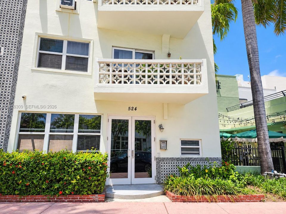 Exterior facade featuring decorative concrete masonry screen walls, private balcony, glass-paneled double entry door, and manicured landscaping with brick edging