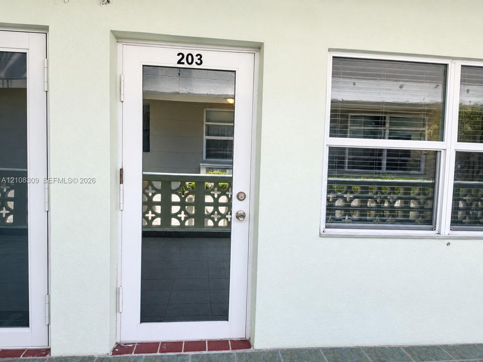 White-framed glass entry door, multi-pane window with integrated blinds, and decorative concrete screen wall