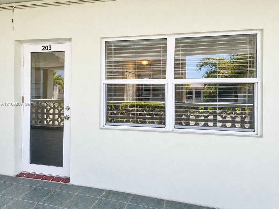 Exterior entrance featuring a white-framed glass entry door, a multi-pane horizontal window with integrated blinds, and tile flooring