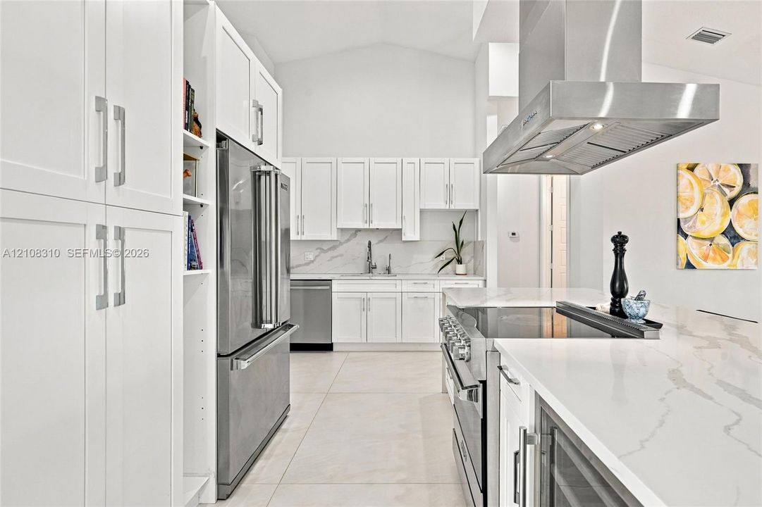 Kitchen featuring shaker-style cabinetry, stainless steel appliances, a stainless steel range hood, stone-finish countertops, and large-format tile flooring