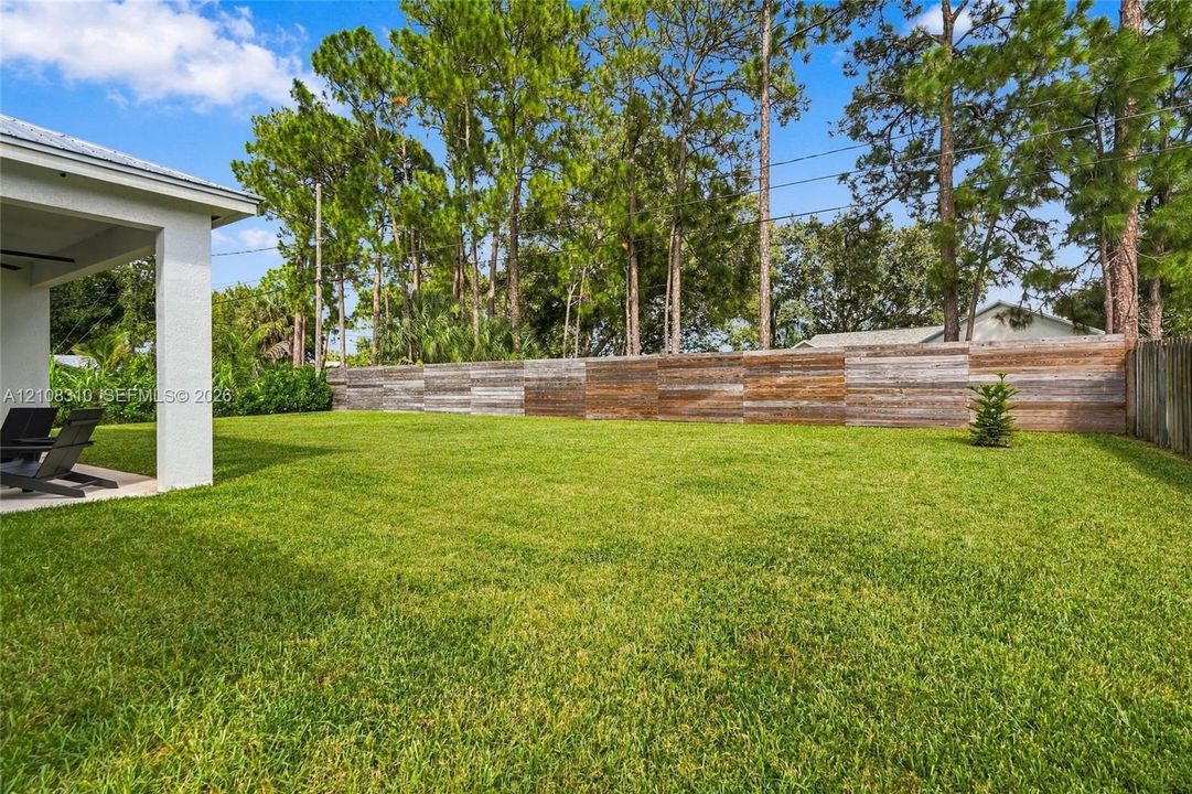 Expansive backyard featuring a covered patio, a manicured lawn, horizontal wood-plank fencing, and mature pine trees