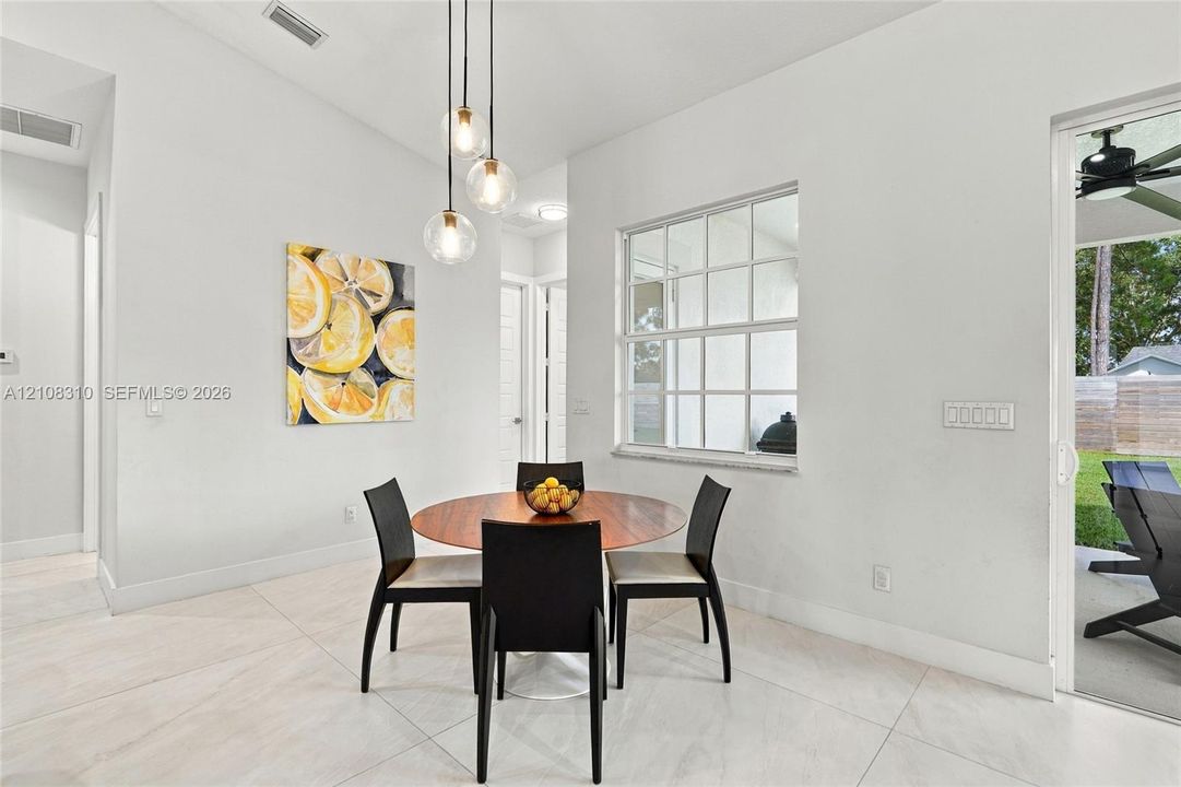 Vaulted ceilings, large-format tile flooring, multi-light globe pendant fixture, and sliding glass door with external patio access