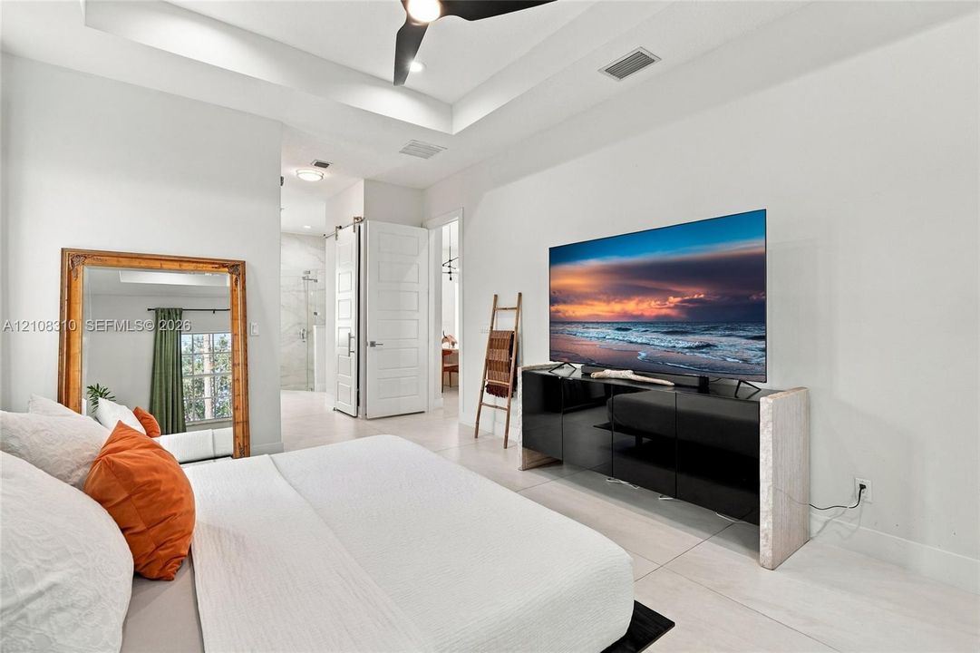 Tray ceiling with integrated recessed lighting, light-toned tile flooring, and a white sliding barn-style door
