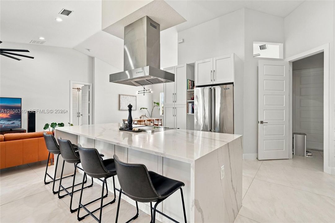 Kitchen featuring a central island with a solid-surface waterfall countertop, stainless steel ceiling-mounted range hood, built-in cabinetry, and tile flooring