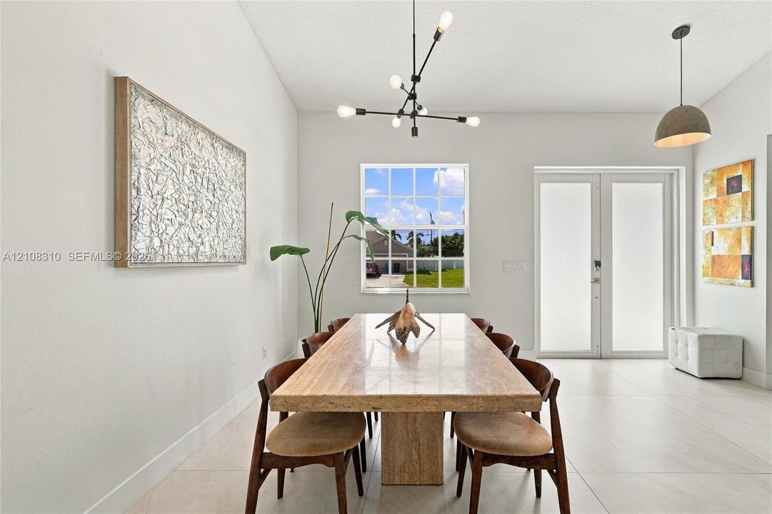 Spacious room featuring large-format tile flooring, multi-light contemporary chandelier, frosted glass double doors, and a grid-pane window
