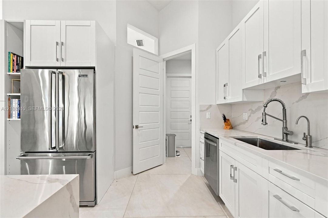 Kitchen featuring white shaker-style cabinetry, stainless steel professional-grade refrigerator, quartz countertops with matching backsplash, and an undermount sink with a high-arch pull-down faucet