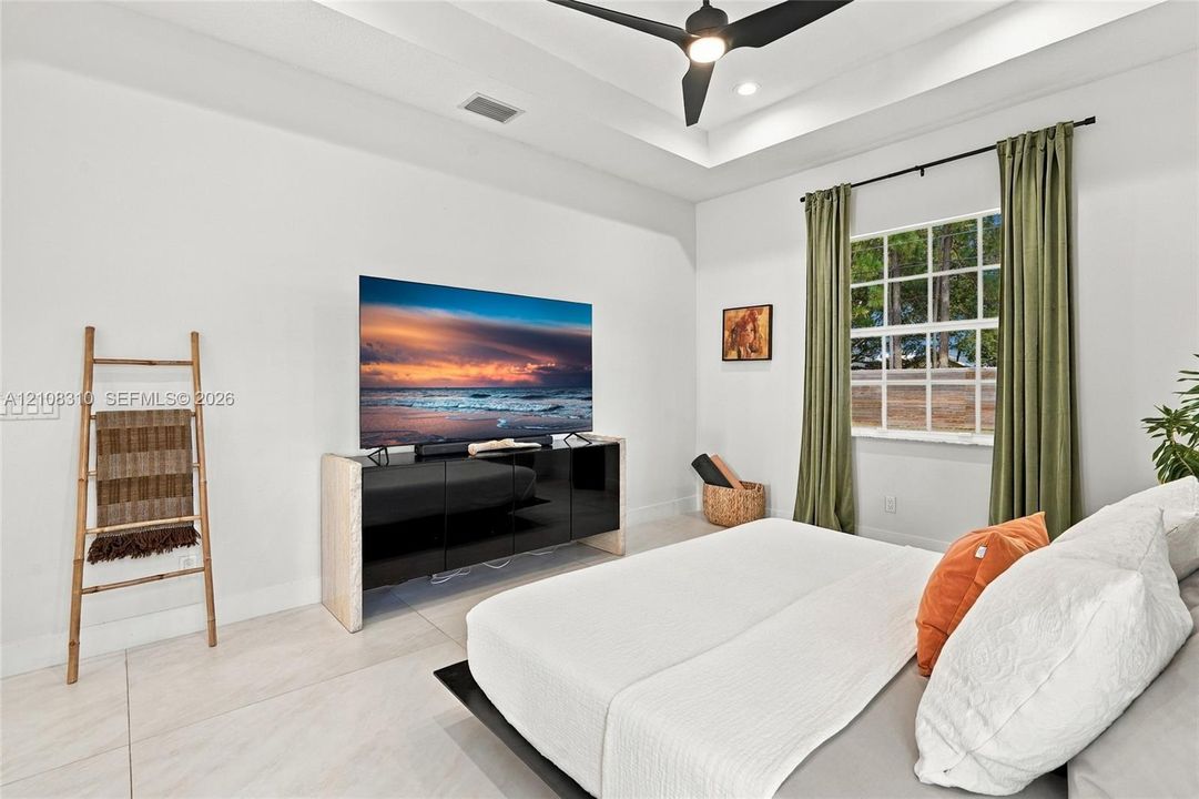 Tray ceiling, large-format tile flooring, multi-pane window, and matte black ceiling fan with integrated lighting