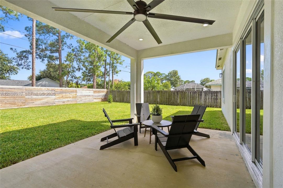 Covered concrete patio featuring a ceiling fan with integrated lighting, recessed lighting, and sliding glass doors, opening to a fenced backyard with grass lawn