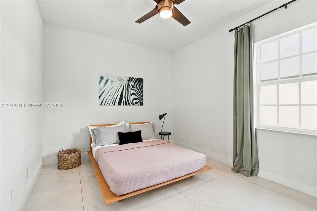 High ceilings featuring a matte bronze finish ceiling fan with integrated lighting, large-format tile flooring, and a multi-pane window with a curtain rod