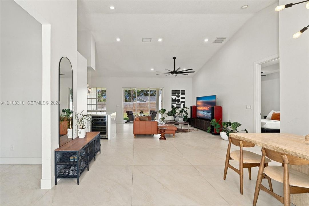 Open-concept interior featuring large-format tile flooring, vaulted ceilings, recessed lighting, a modern ceiling fan, and a built-in wine refrigerator