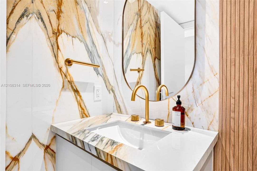 Wall-mounted vanity featuring large-format stone-patterned tile wall cladding, an integrated undermount sink, brass-finish widespread faucet, arched vanity mirror, and wood-slat accent paneling