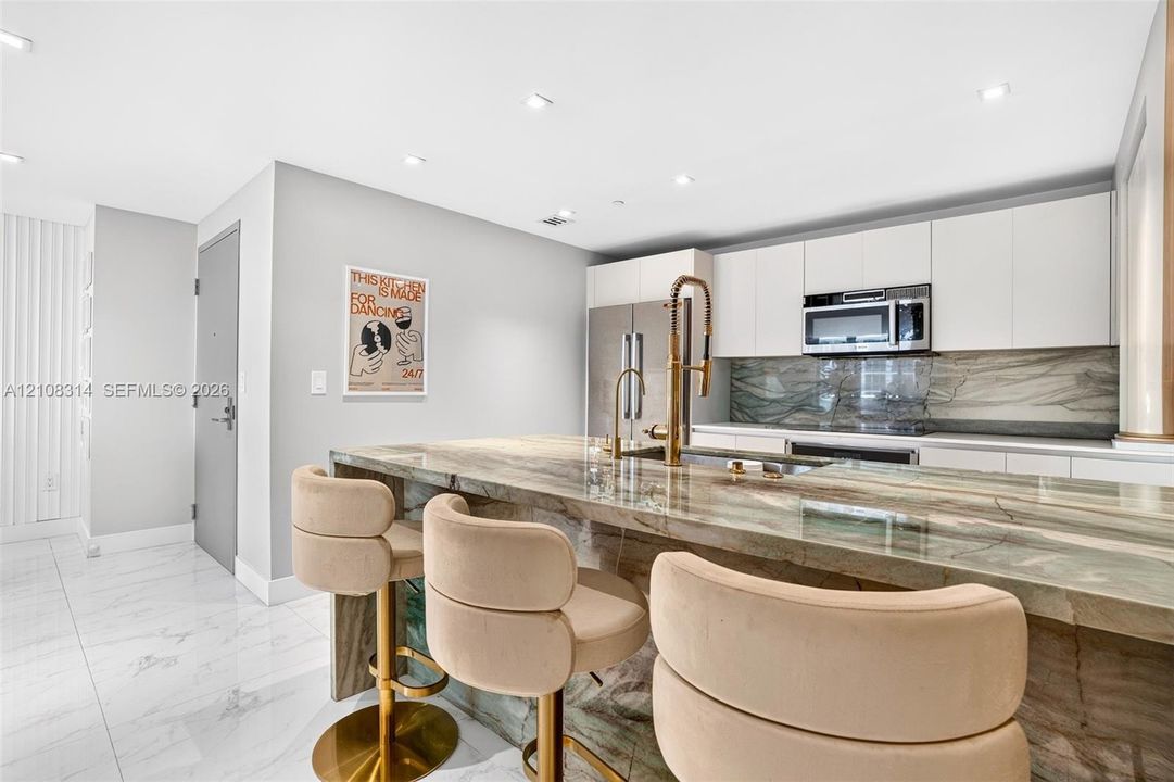 Kitchen featuring a stone waterfall island with a metal gooseneck faucet, white flat-panel cabinetry, a matching stone backsplash, stainless steel appliances, and large-format tile flooring