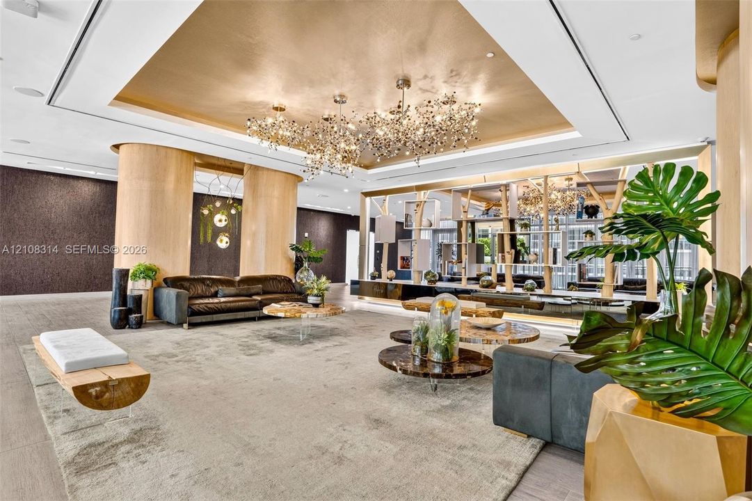 Metallic tray ceiling, large-scale multi-bulb crystal chandeliers, curved light-wood structural columns, integrated architectural shelving, and recessed lighting