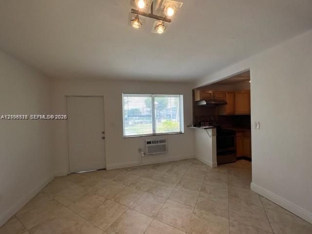 Neutral-toned tile flooring, four-light flush-mount ceiling fixture, and large single-hung window with an integrated wall-mounted air conditioning unit