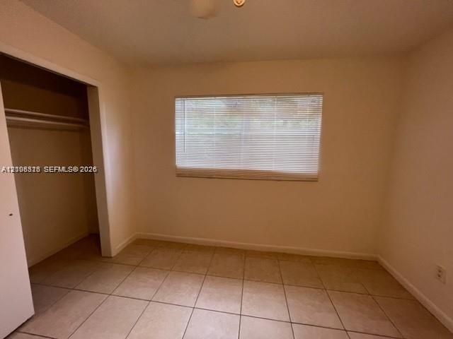 Neutral-toned tile flooring, recessed closet with built-in hanging rod, and window with integrated horizontal blinds