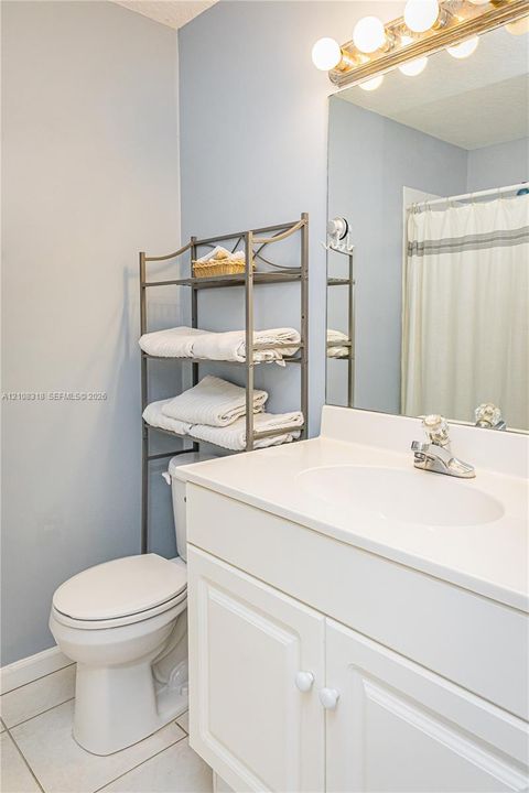Bathroom vanity featuring a white cabinet base, solid surface countertop with integrated basin, polished metal faucet, wall-mounted mirror, and multi-bulb fixture