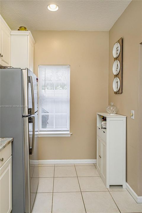 Kitchen featuring tile flooring, white shaker-style cabinetry, stainless steel refrigerator, and recessed ceiling lighting