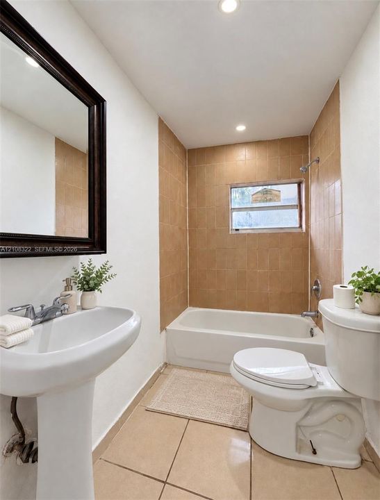 Bathroom featuring a pedestal sink, framed wall mirror, tiled bathtub surround, and tile flooring