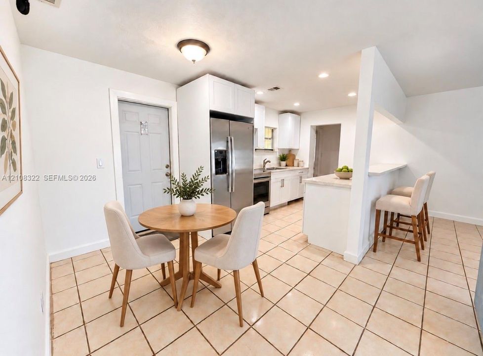 Kitchen featuring white shaker-style cabinetry, stainless steel refrigerator, stone-surfaced breakfast bar, and light-toned floor tiling