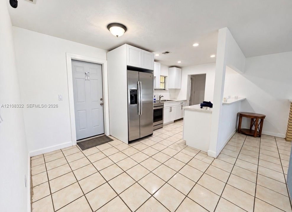 Kitchen featuring white cabinetry, stainless steel appliances, ceramic tile flooring, and a breakfast bar