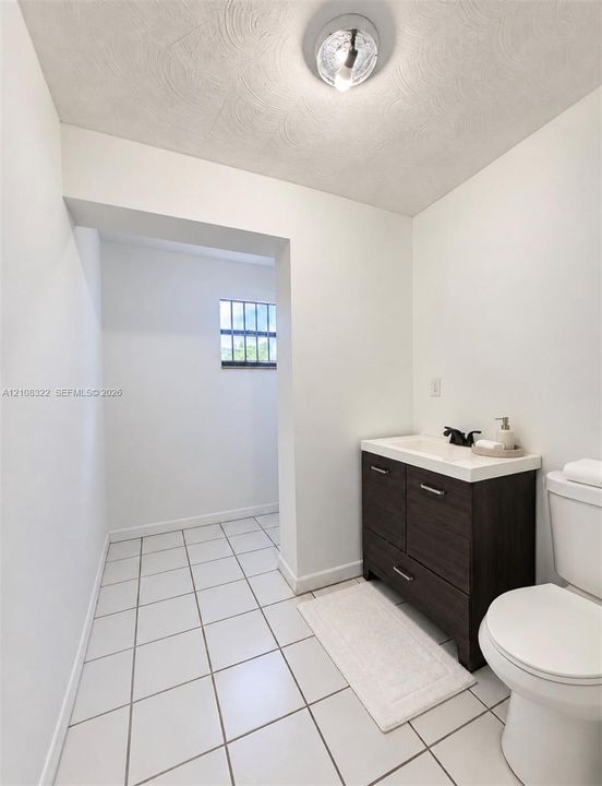 Dark wood-finish vanity with a white countertop and matte black faucet, ceramic tile flooring, and flush-mount ceiling lighting