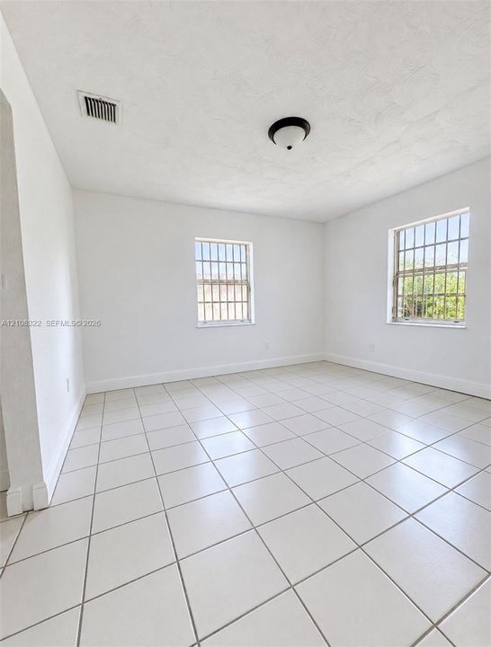 Neutral interior space featuring large-format ceramic tile flooring, two windows with metal security bars, and a central flush-mount ceiling fixture