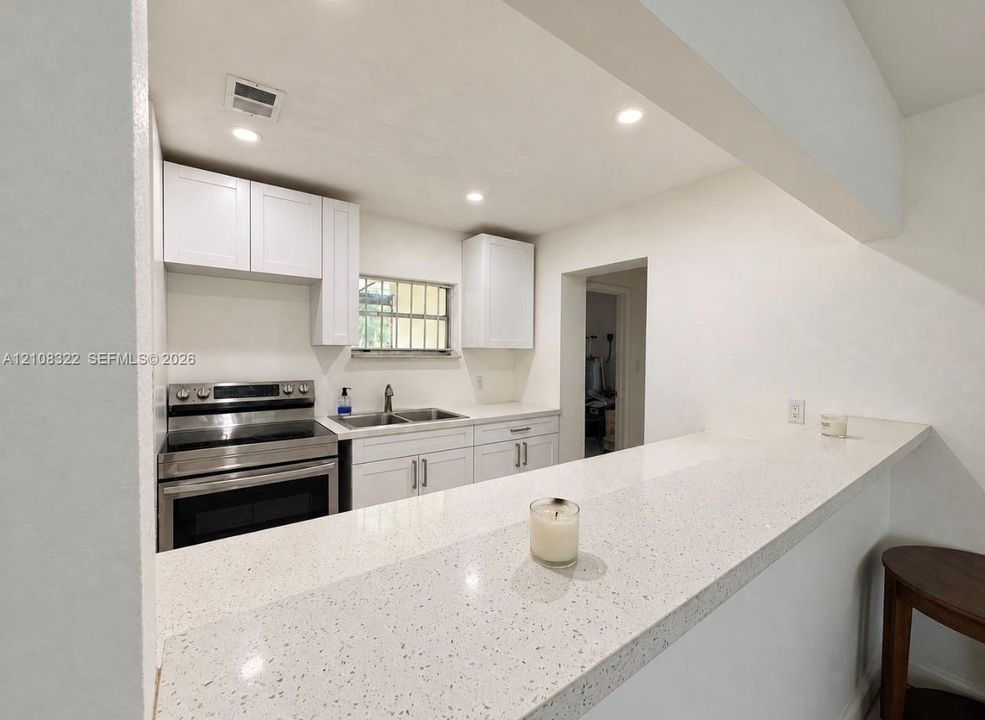 Kitchen featuring white cabinetry, quartz countertops, a dual-basin stainless steel sink, and stainless steel range