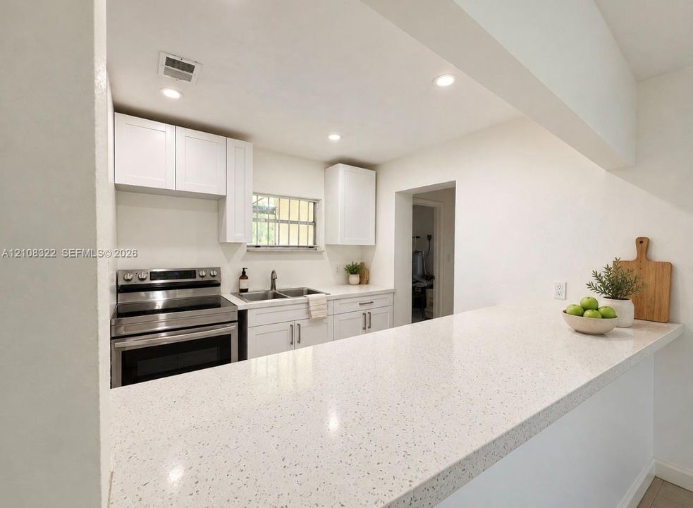 Kitchen featuring white shaker-style cabinetry, a quartz countertop breakfast bar, recessed lighting, and stainless steel appliances