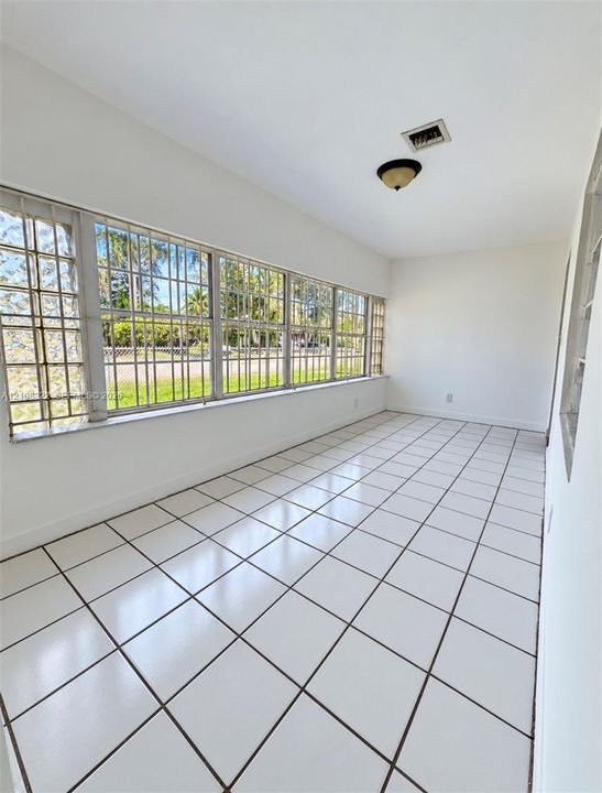 Enclosed space featuring square ceramic tile flooring, an expansive wall of multi-pane windows with metal security bars, glass block side accents, and a flush-mount ceiling light fixture