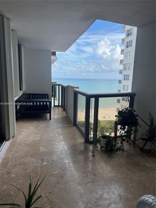 Covered balcony featuring stone flooring and a glass-paneled railing