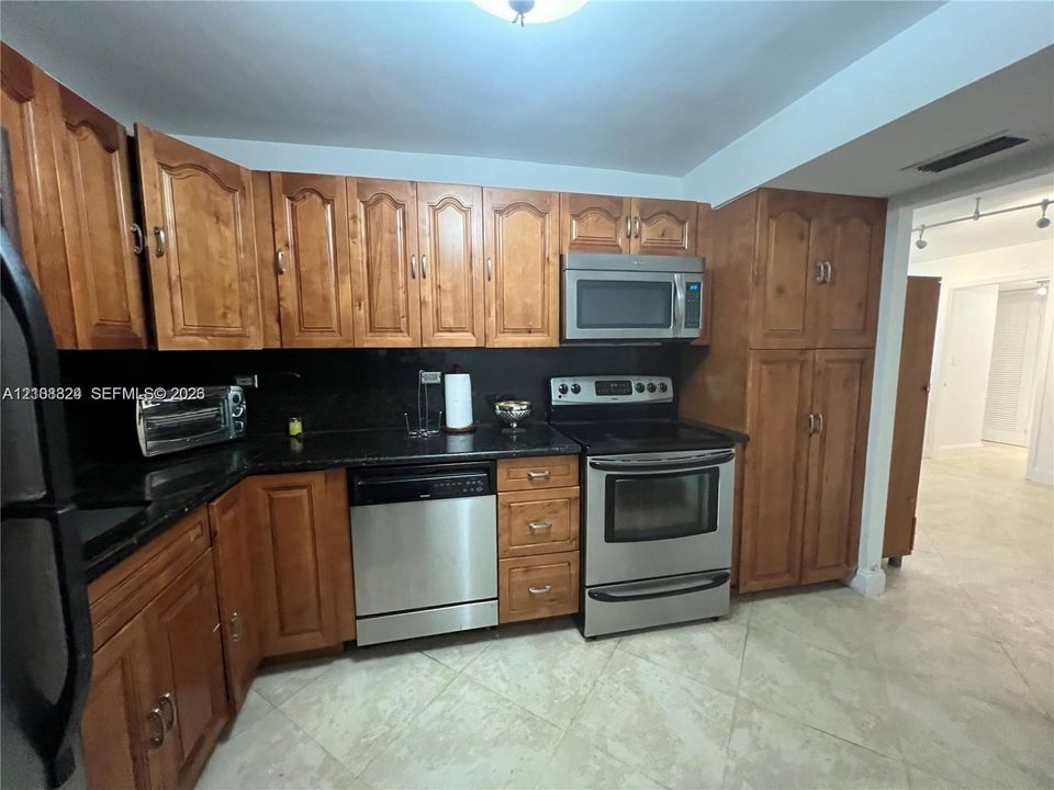 Kitchen featuring stained wood cabinetry, stone countertops, and stainless steel appliances including a built-in microwave, range, and dishwasher