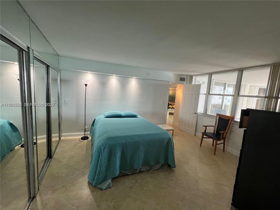 Spacious room featuring floor-to-ceiling mirror-paneled closet doors, neutral tile flooring, built-in recessed ceiling lighting, and a wall of large windows