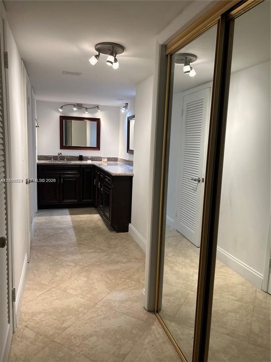 Dark-finish built-in vanity with a light-toned countertop, tile flooring, mirrored sliding closet doors, and multi-directional track lighting