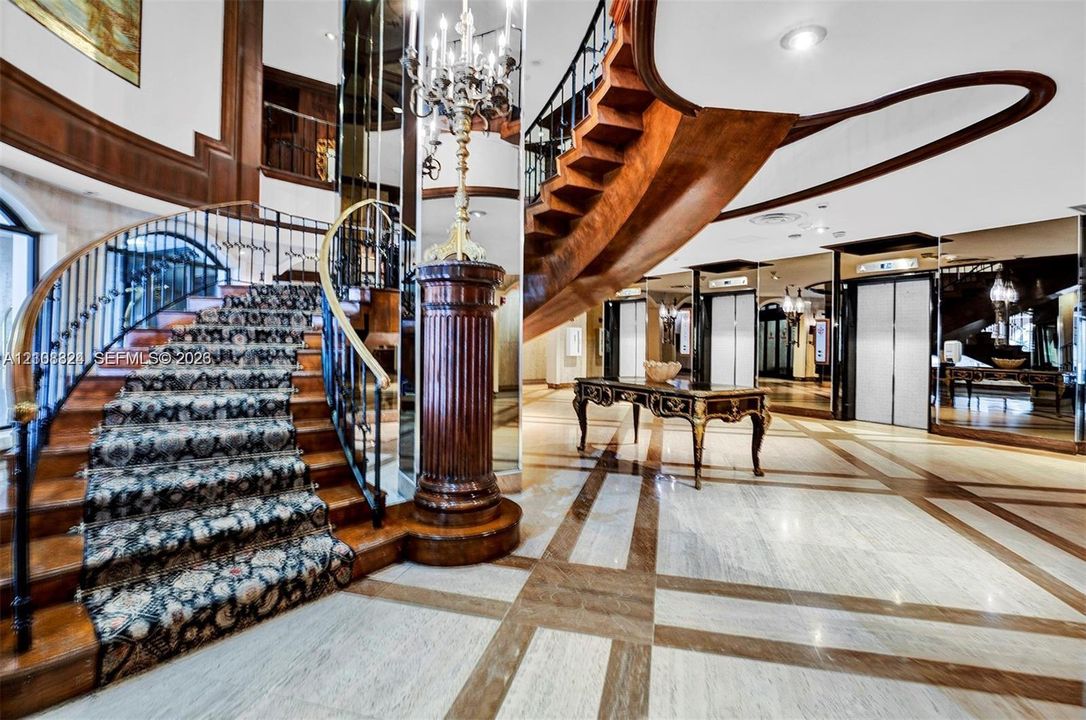 Grand foyer featuring a dual-tone stone floor, a sweeping staircase with custom metal railing, full-height wall mirrors, and recessed lighting