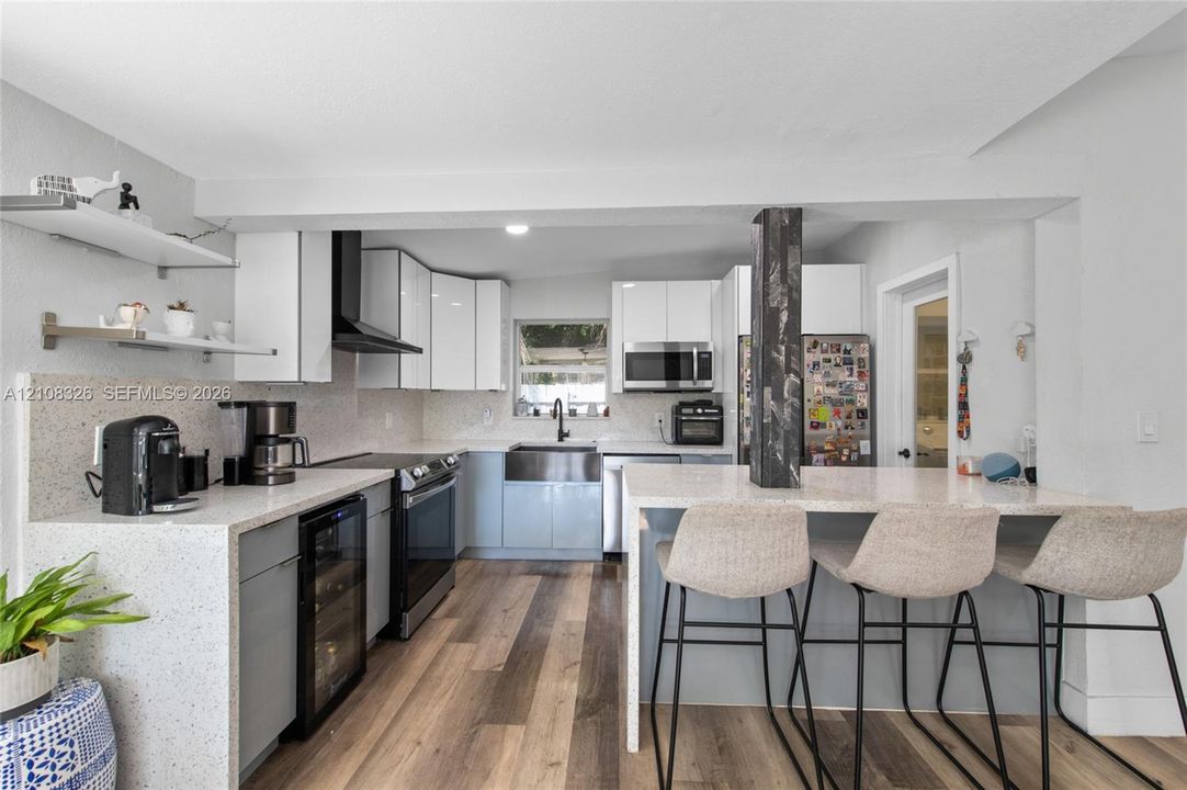 Kitchen featuring flat-panel cabinetry, quartz countertops with waterfall edge, apron-front stainless steel sink, built-in beverage refrigerator, and wood-finish flooring