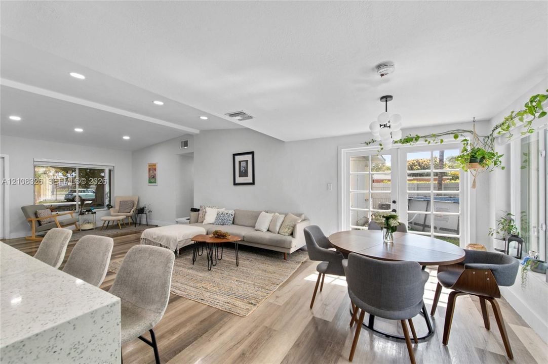 Open-concept interior featuring wood-finish flooring, recessed lighting, a modern multi-globe chandelier, and double French doors providing exterior access