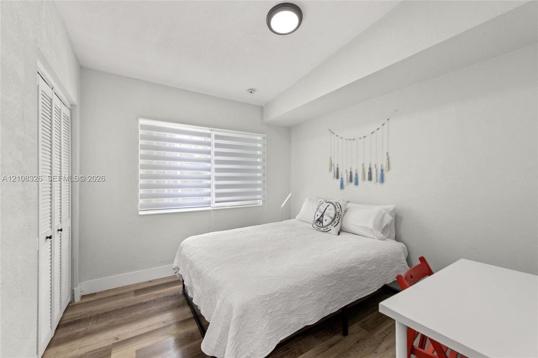 Neutral-toned room featuring wood-finish flooring, dual-pane windows with adjustable roller shades, and floor-to-ceiling closet with louvered bi-fold doors